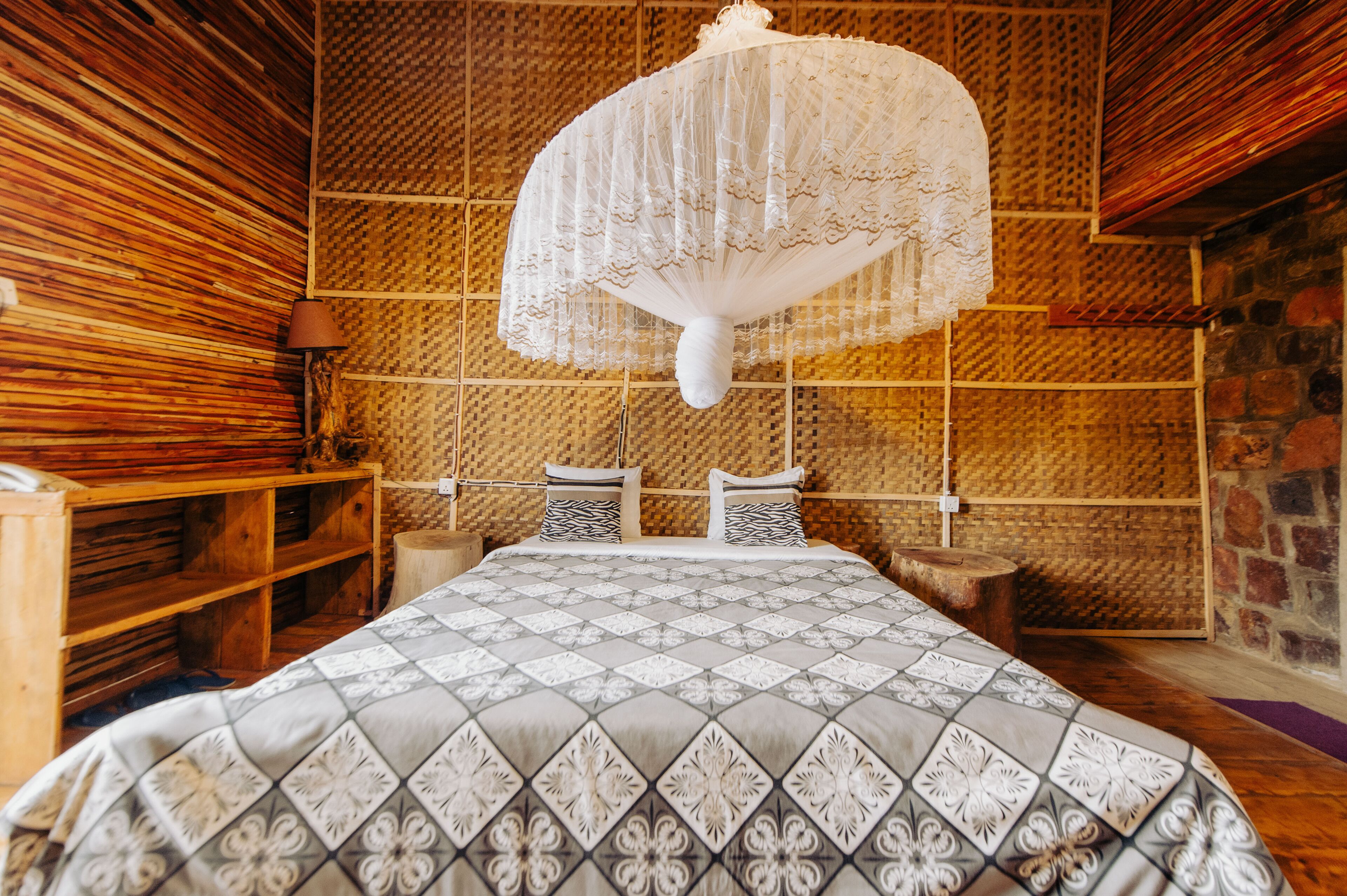 A room with a bed, wooden shelves, a woven wall, and a hanging light fixture.