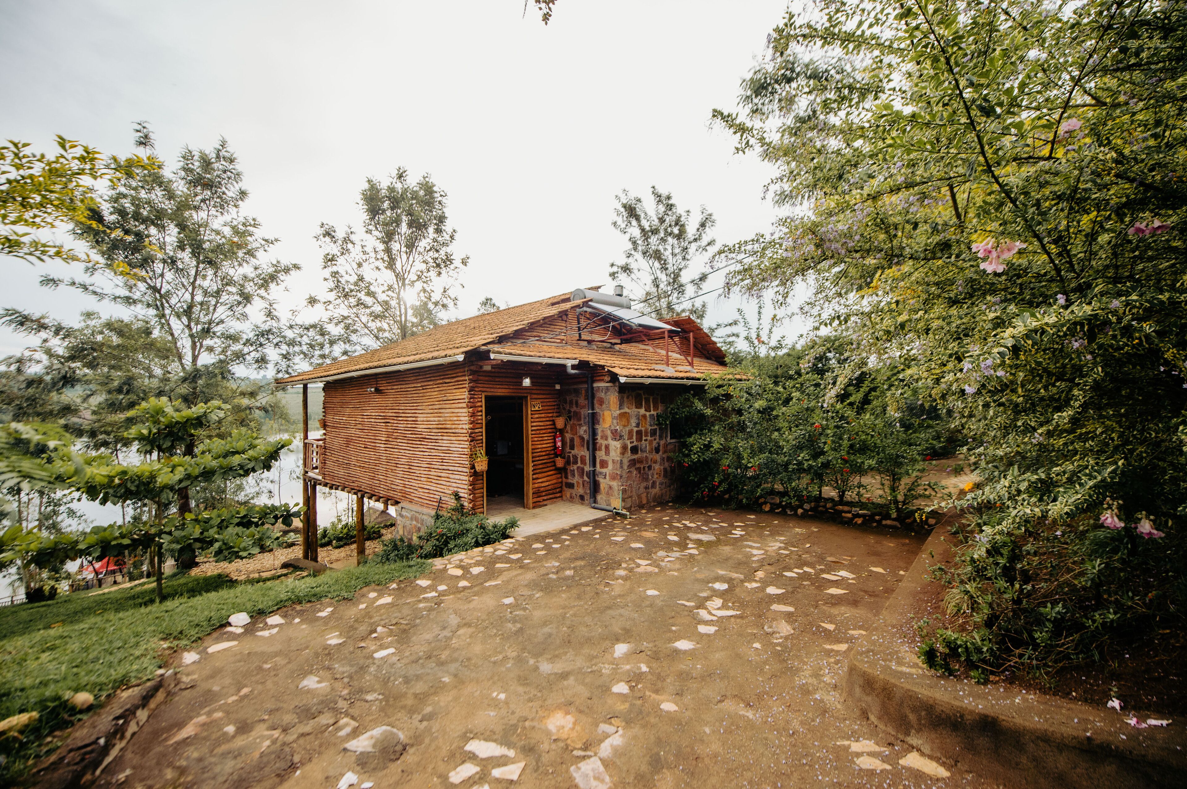 A rustic wooden house with a stone foundation, a tiled roof, and a paved entrance.