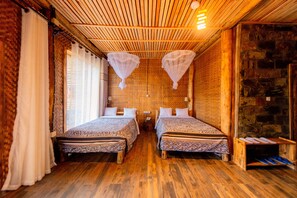 A room with two beds, wooden flooring, a stone wall, and a wooden ceiling with hanging lights.