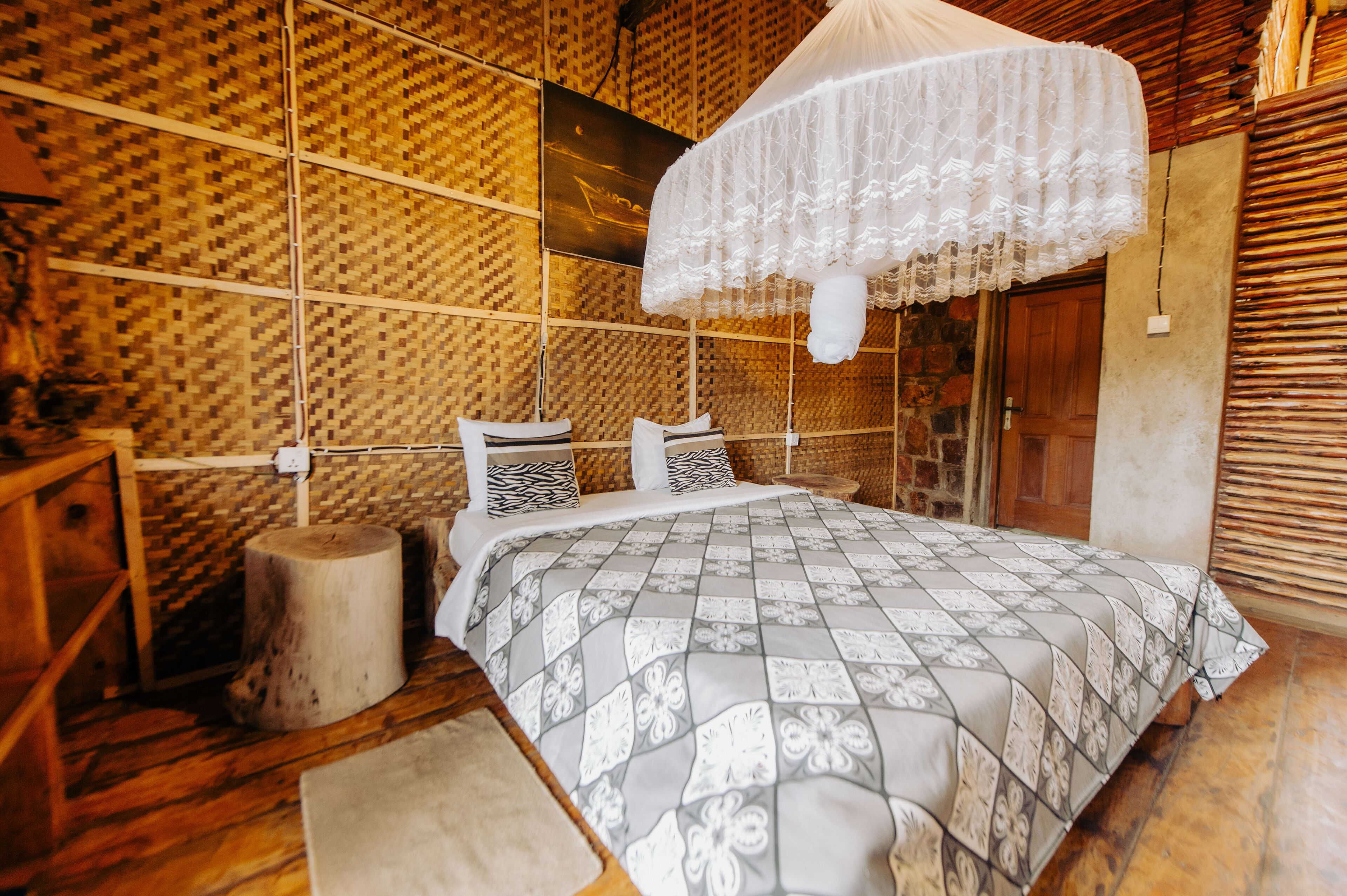 Un dormitorio con una cama, suelo de madera, pared tejida y dosel.