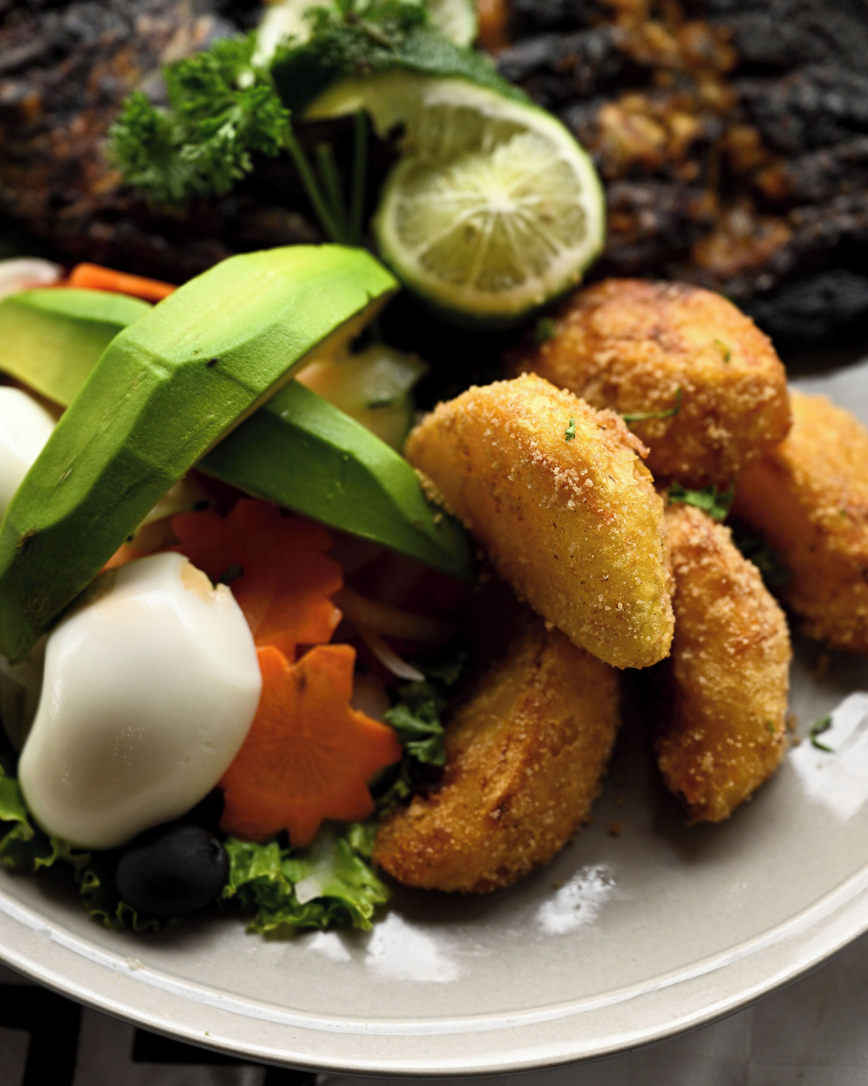 A plate with fried food, avocado, a lime wedge, and a dollop of sauce.