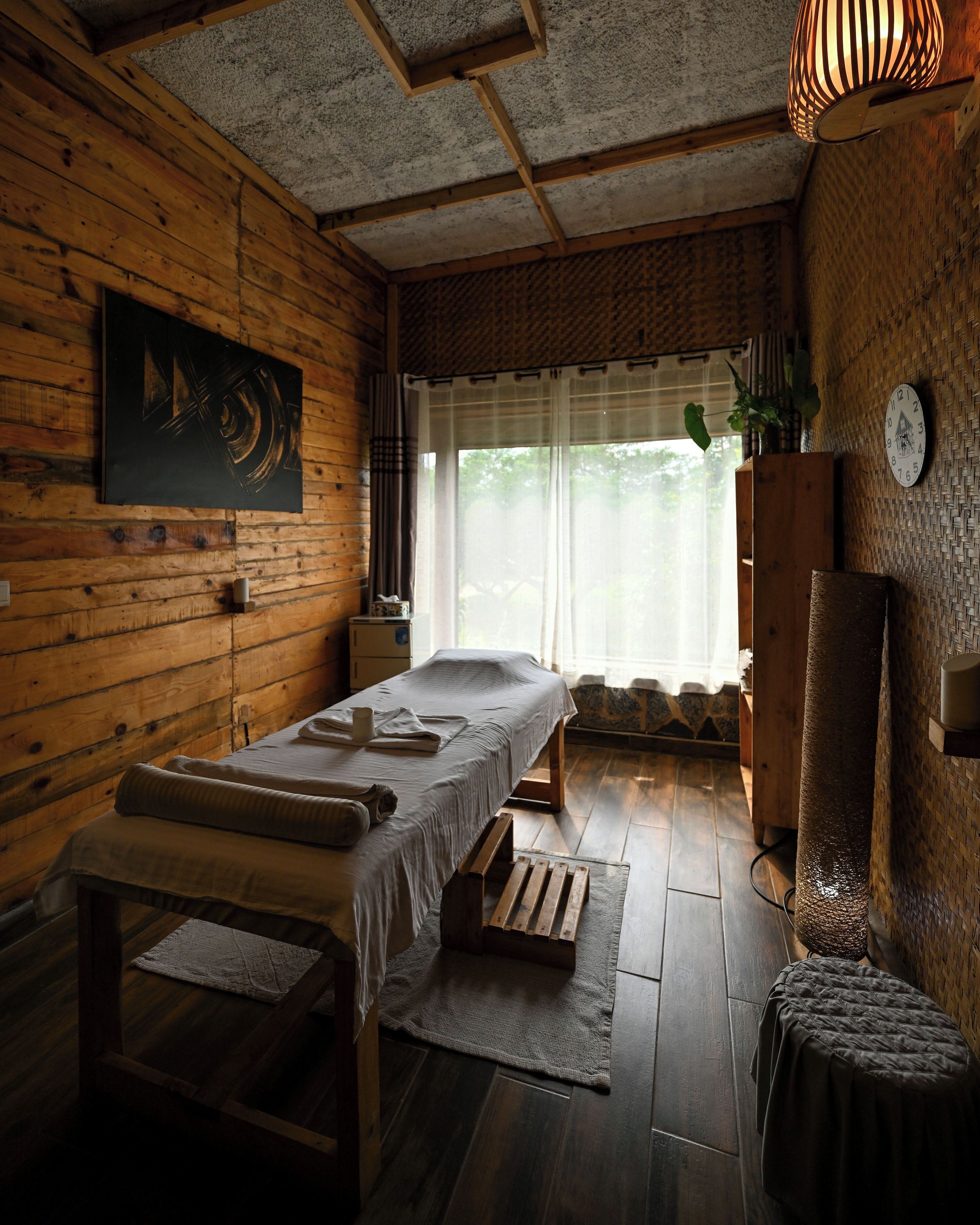 Una habitación de madera con una cama, una camilla de masaje, un mueble pequeño y un reloj de pared.