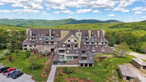 Ein mehrstöckiges Hotel mit einem zentralen Uhrturm, umgeben von üppiger Vegetation und Bergen im Hintergrund.