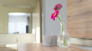 En genomskinlig glasvas med rosa blommor står på ett träbord bredvid ett dekorativt glashållare för ljus.