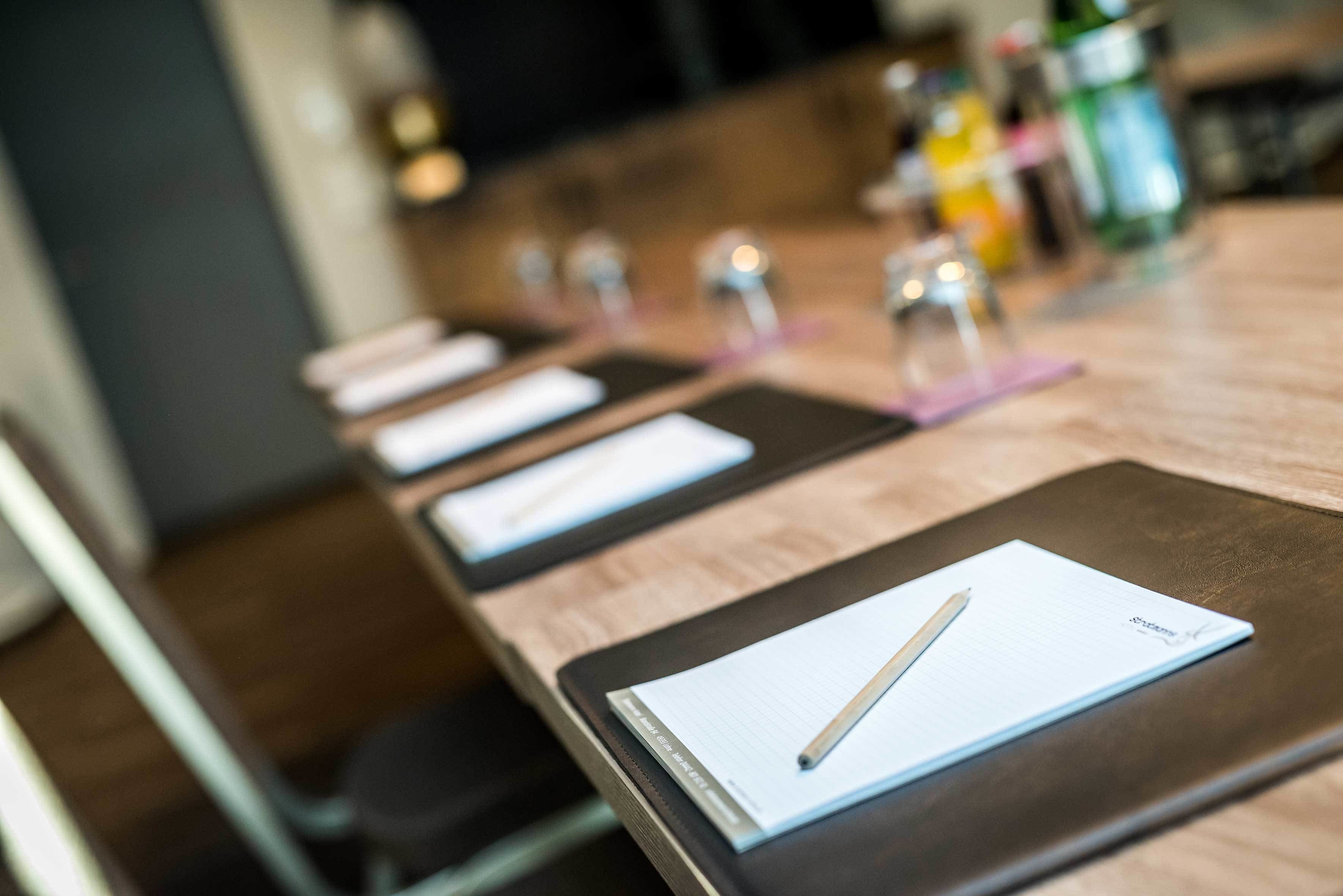 Ein Konferenztisch mit Notizbuch, Stift und einer Wasserflasche im Hintergrund.