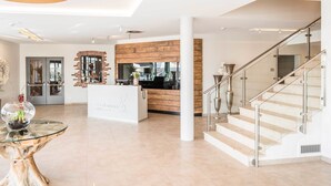 Un hall de hotel con mostrador de recepción, una escalera y un ventanal grande.