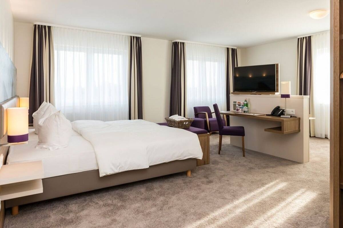 Una habitación de hotel con una cama, un escritorio con computadora, un televisor y una silla.