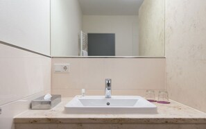A bathroom with a white sink, a mirror, and a towel dispenser. - Stratmanns Hotel (Lohne)