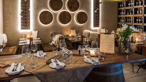 Un restaurante con una larga mesa dispuesta para comer, un atril con la carta y una estantería para vinos al fondo.