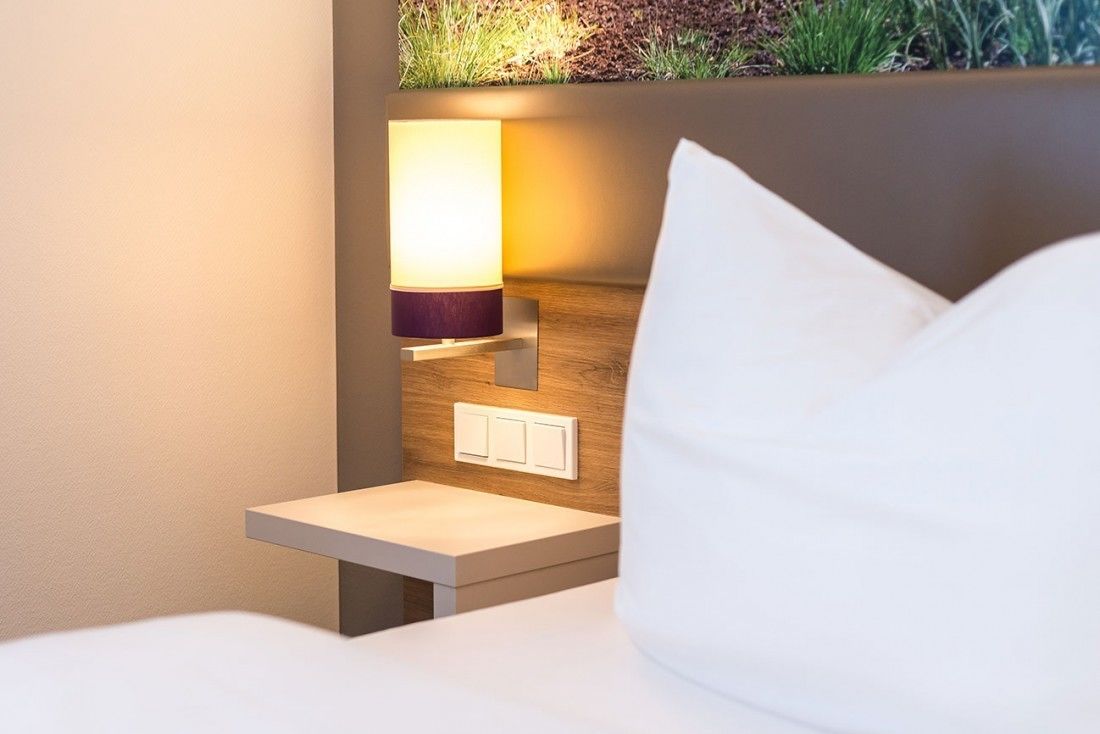 Una cama bien hecha con un cojín blanco y una mesita de noche con una lámpara.