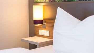 Una cama bien hecha con un cojín blanco y una mesita de noche con una lámpara.