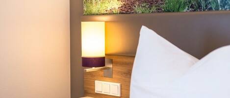 A neatly made bed with a white pillow and a bedside table with a lamp.