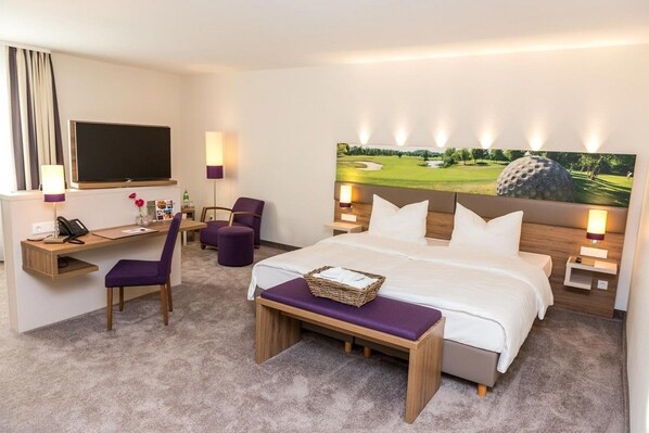 A hotel room with a bed, a desk, a chair, a TV, and a golf-themed painting on the wall. - Stratmanns Hotel (Lohne)