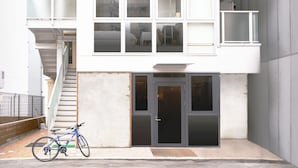 A modern building with a staircase leading to a balcony, a bicycle parked in front, and a door with a glass panel.