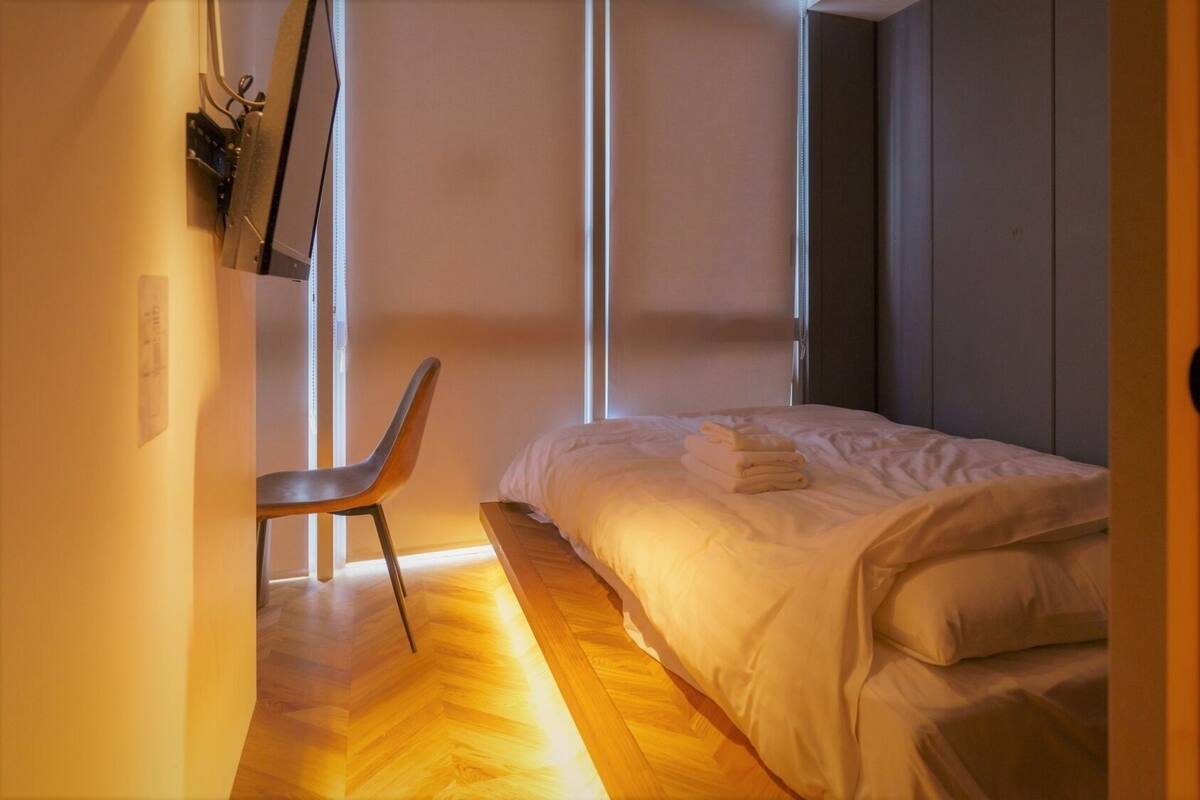 A small, modern bedroom with a bed, a chair, and a window.