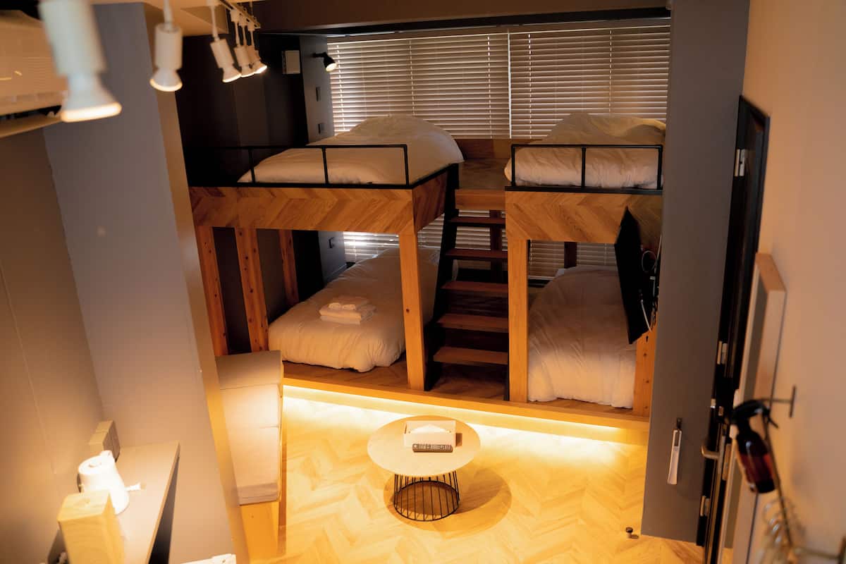 A compact room with bunk beds, a small table, and a window with blinds.