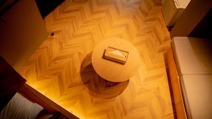 A wooden herringbone floor with a round table and a white refrigerator in the background.