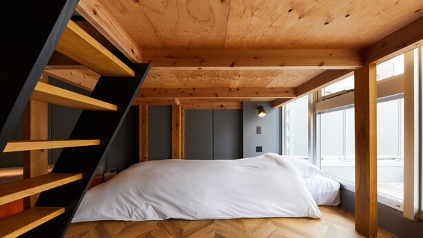 A bedroom with a wooden staircase, a bed with white bedding, and large windows.