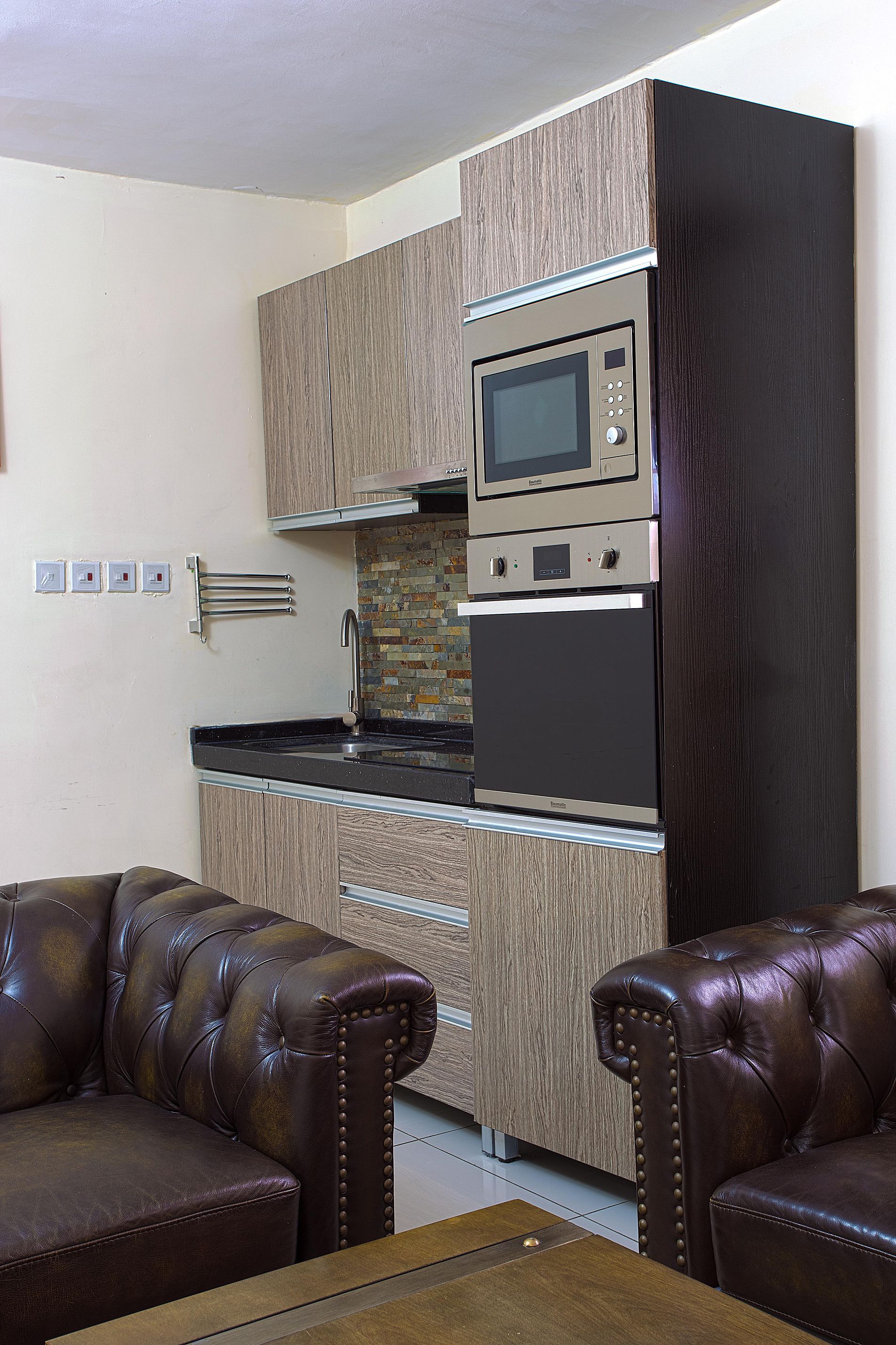 Une cuisine compacte dotée d’appareils électroménagers intégrés, un coin repas avec un canapé en cuir et un mur d’accent de couleur foncée.