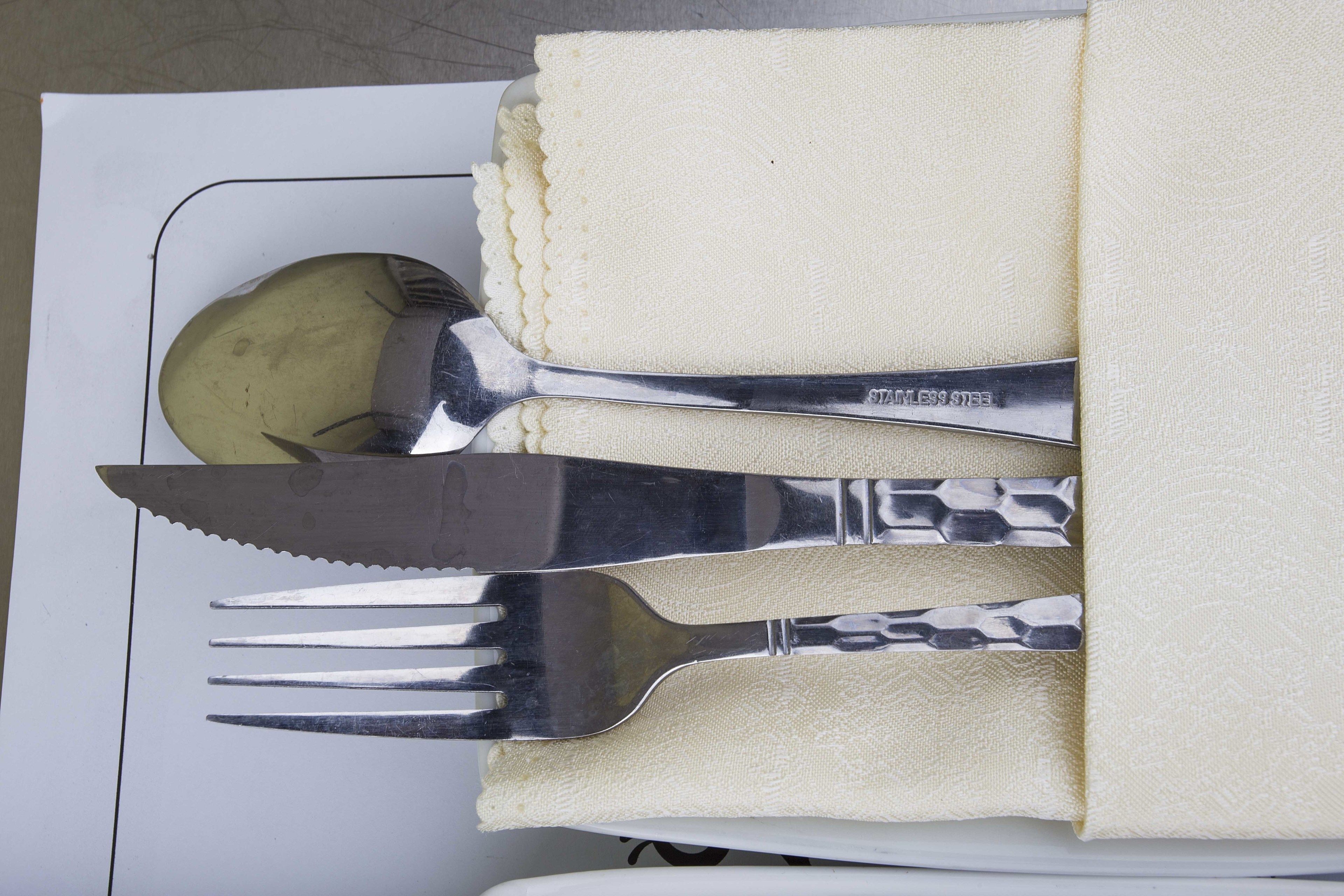 A neatly arranged set of silverware on a white plate with a folded napkin.