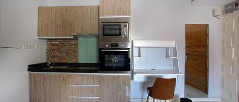 A compact kitchen with a microwave, oven, and a small dining area with a chair.