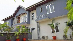 A two-story house with a balcony, potted plants, and an air conditioning unit. - H21 Apartments & Lounge (Lekki)