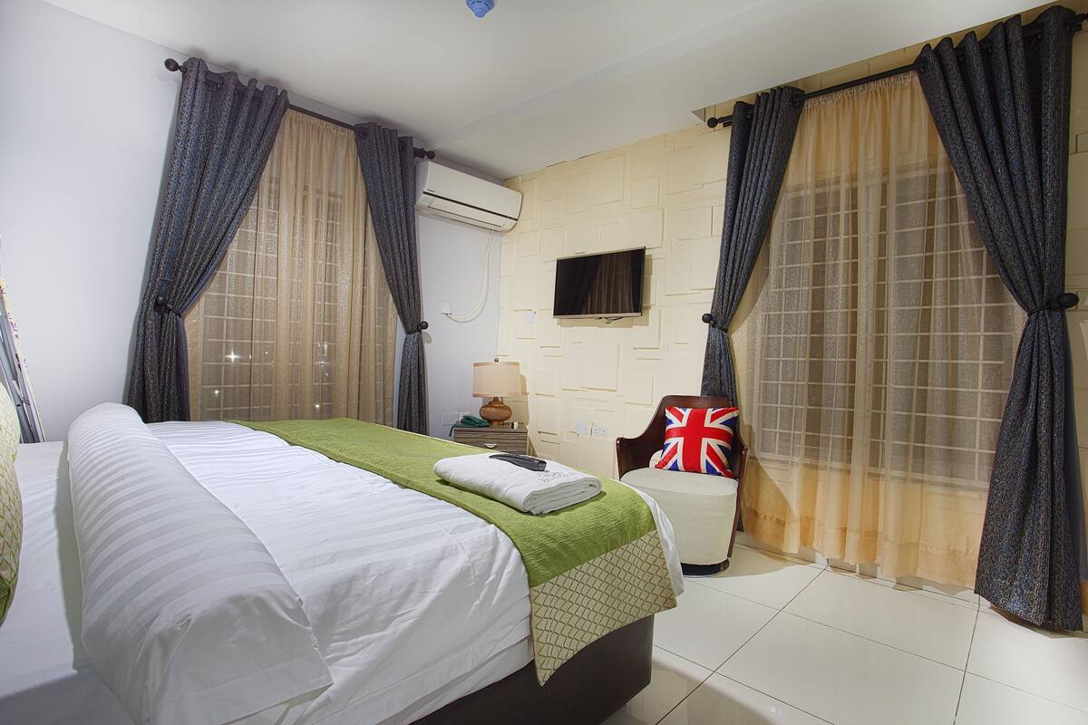 Ein Hotelzimmer mit Bett, Sessel, Fernseher und Vorhängen.