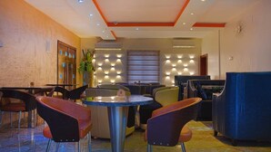 A hotel lobby with a round table, multiple chairs, a blue sofa, and a decorative wall with lights. - H21 Apartments & Lounge (Lekki)