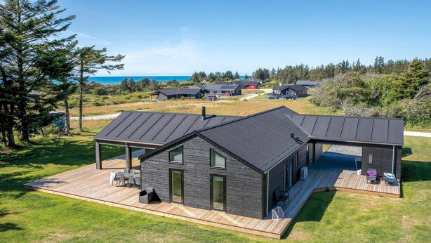 Una casa moderna con terraza de madera, un espacio de estar al aire libre cubierto y vista al océano.