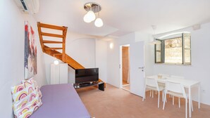 Une chambre à coucher comprenant un lit, un téléviseur, un escalier, un coin repas avec des chaises et une table, ainsi qu’une fenêtre donnant sur un paysage agréable.