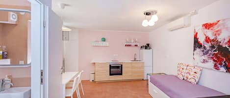 A compact living space with a kitchenette, a bed with a purple bedspread, and a large abstract painting on the wall.