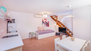 Un espace de vie compact comprenant un coin cuisine, un lit avec des tiroirs de rangement, un coin repas et un escalier.