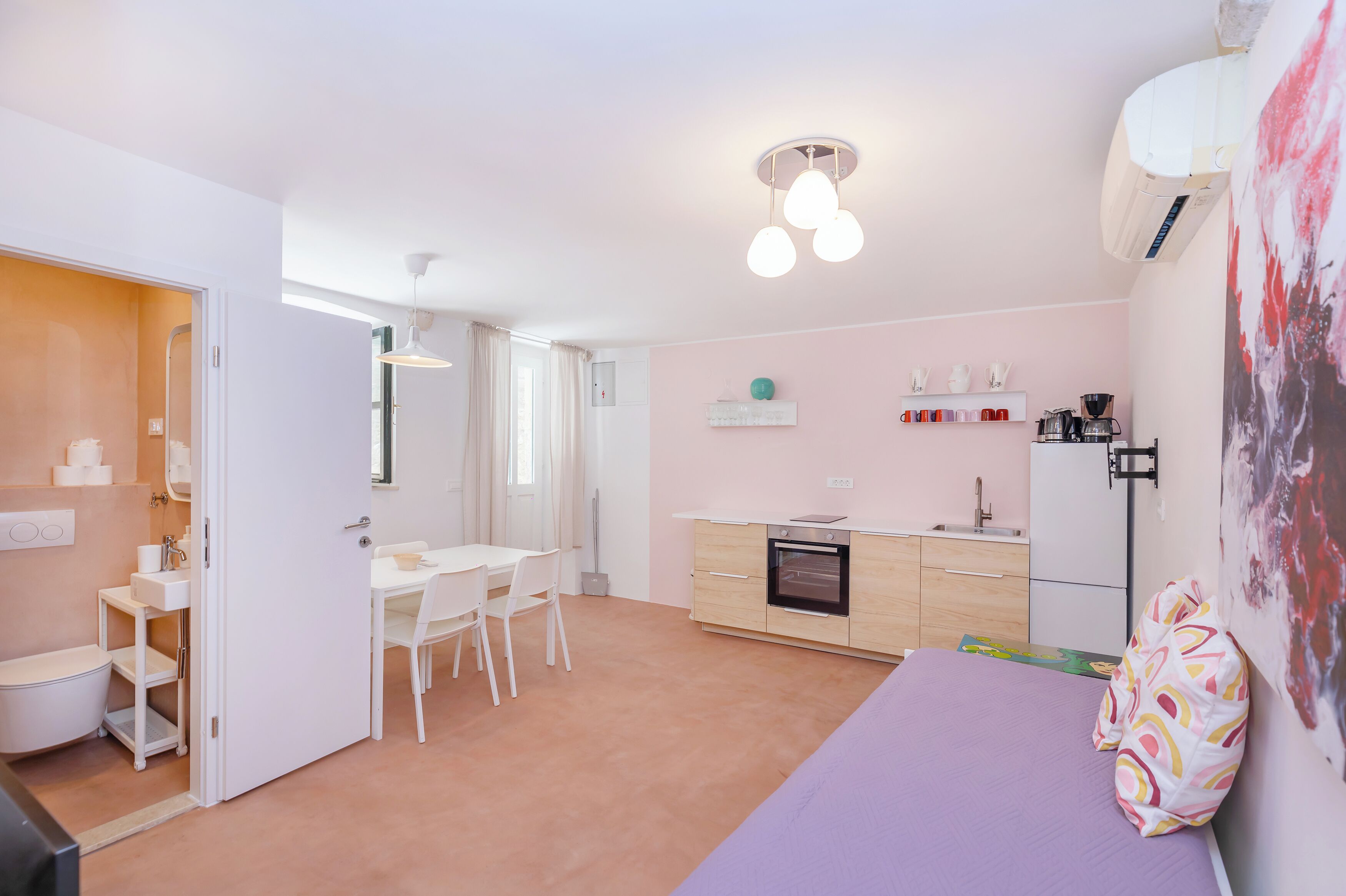 A compact room with a bed, a small kitchenette, a dining area, and a bathroom.