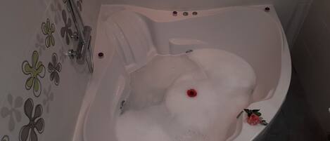 Eine Badewanne mit Schaum, einer Rose und einem Wasserhahn.