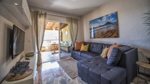 Ein modernes Wohnzimmer mit einem grauen Sofa, einem Flachbildfernseher und einem Gemälde, das eine Strandansicht zeigt.