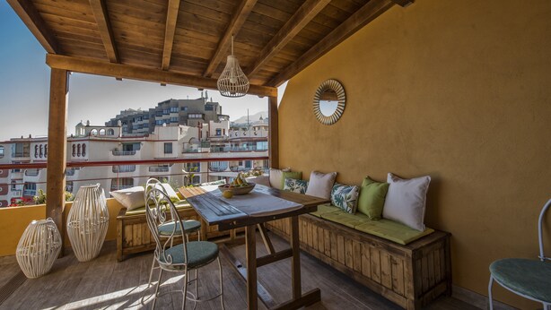 Eine Holzterrasse mit Tisch und Stühlen, einer gepolsterten Bank und einer hängenden Leuchte.
