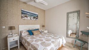 Ein Schlafzimmer mit Bett, Nachttischen, Deckenventilator, Gemälde, Spiegel und einem Sessel.