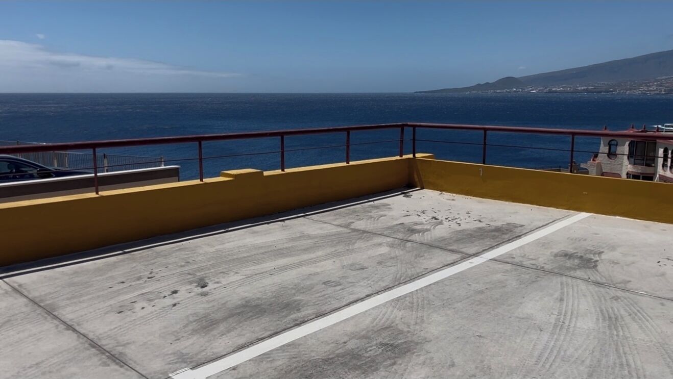 A balcony with a yellow wall and red railing overlooking the sea.
