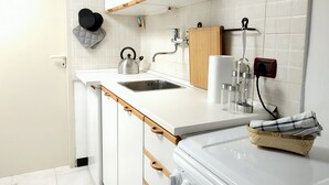 A modern kitchen with white cabinetry, a stainless steel sink, a kettle, and a wooden cutting board. - Holiday Apartment in Genova Fieno (Genoa)