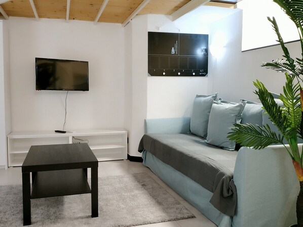 A modern living room with a flat-screen TV, a dark coffee table, a light blue sofa, and a wall-mounted clock.
