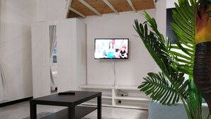 A modern living room with a black coffee table, a television mounted on the wall, and a large green plant in a white pot. - Holiday Apartment in Genova Fieno (Genoa)