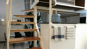 A modern interior with a spiral staircase, wooden shelves, a kitchen area, and a dining space. - Holiday Apartment in Genova Fieno (Genoa)