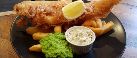 A plate with fish and chips, a lemon wedge, mushy peas, and tartar sauce.