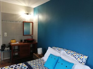 Relax in this stylish bedroom with a large bed, geometric patterned bedspread, and a nightstand with a lamp and sink.