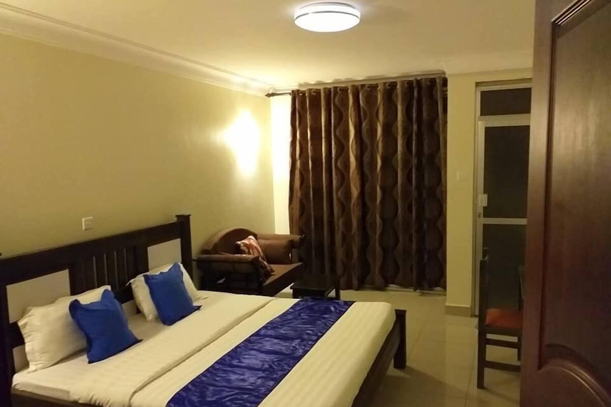 A hotel room with a bed, a chair, a curtain, and a door.