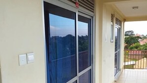 Un balcon donnant sur un quartier résidentiel, une porte-fenêtre coulissante et un sol carrelé.