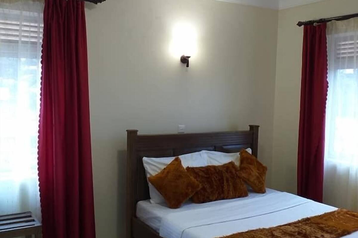 A neatly made bed with a wooden headboard, red curtains, and a wall-mounted light fixture.