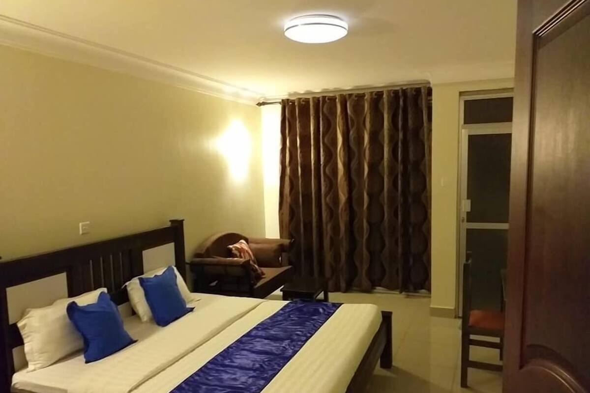 A hotel room with a bed, a chair, a curtain, and a door.