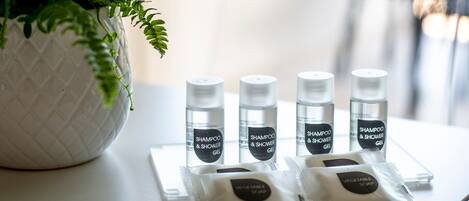 A table with four bottles of shampoo and shower gel, and two packets of vegetable soap.