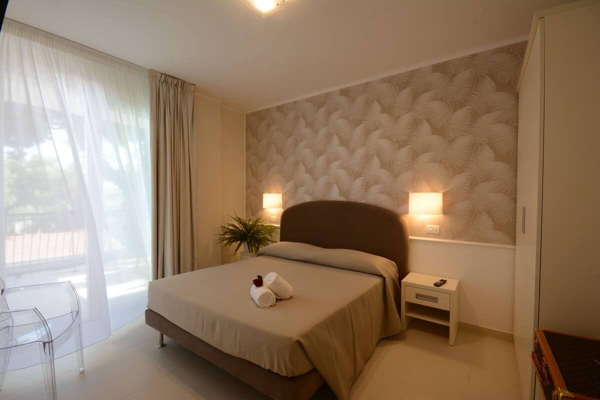 A bedroom with a bed, bedside tables, a nightstand, a chair, and a window with curtains.